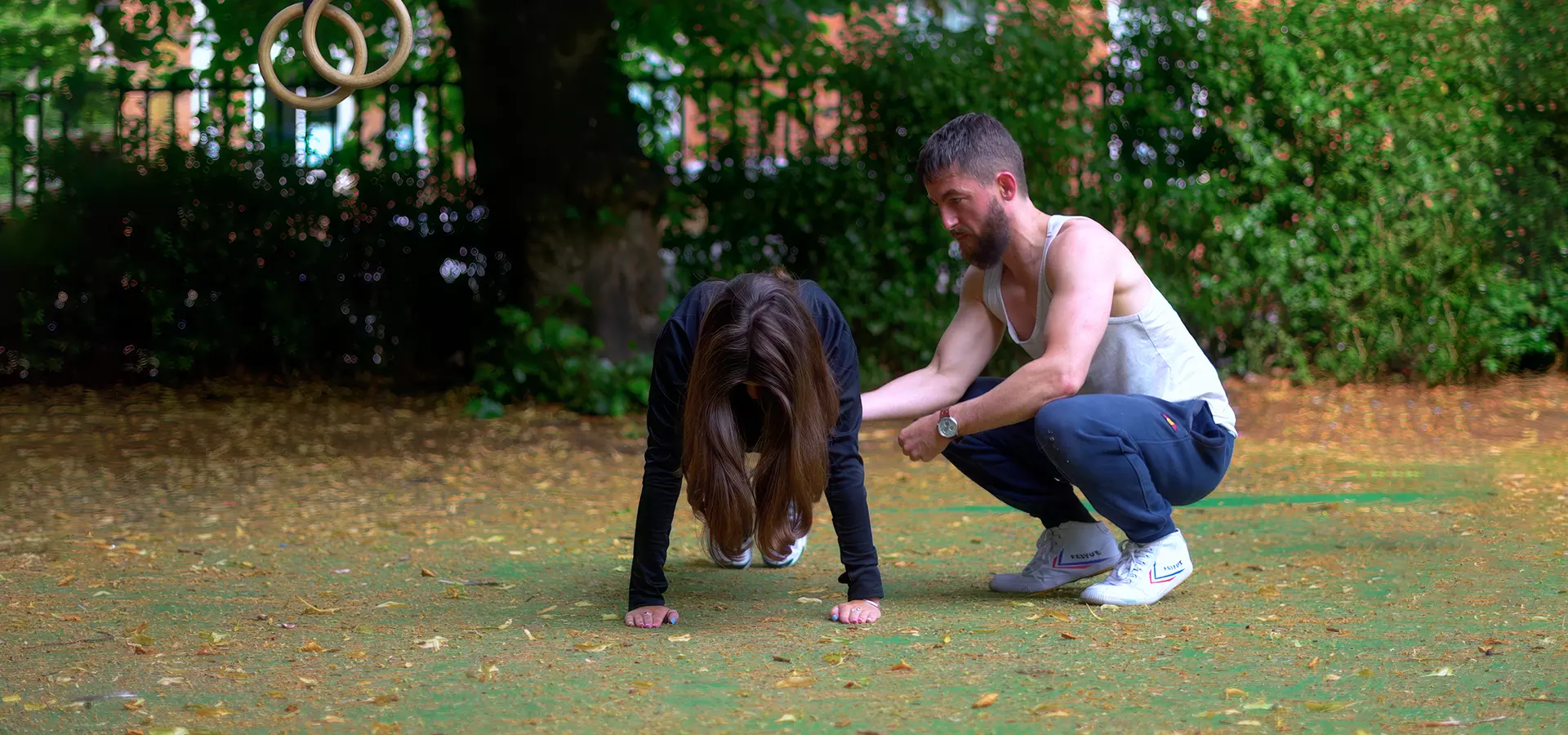 Personal trainer guiding a client's form during a bodyweight gymnastic ring exercise in Glasgow